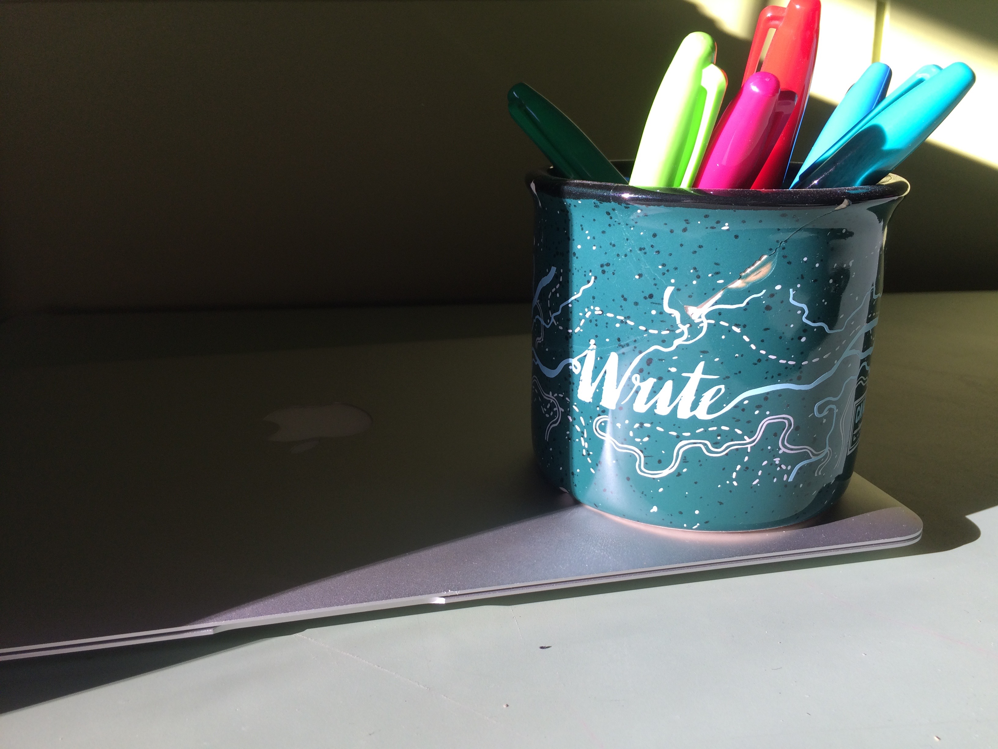 markers in a mug on top of laptop